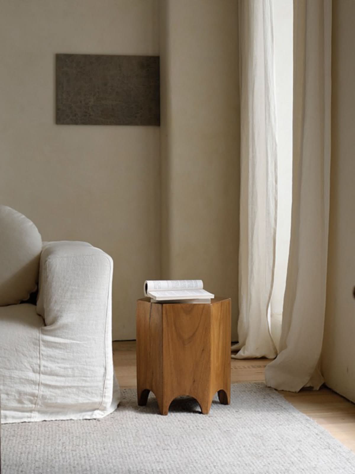 Minimalist wooden hexagonal side table with book on top, beside a white sofa.